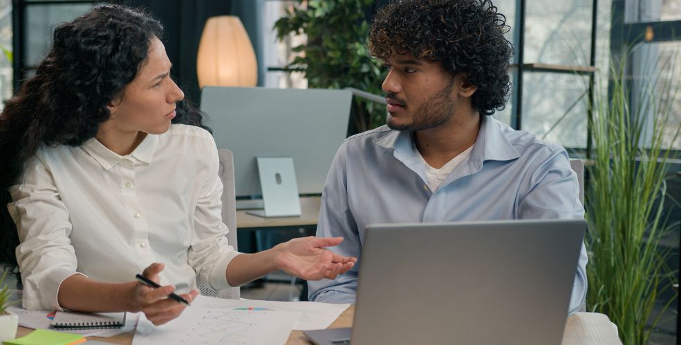 A woman explaining a concept to a man in a professional setting, symbolizing engaged learning and understanding over memorization.