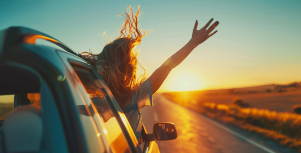 A young woman leans out of a car window, arms outstretched, hair flowing in the wind as she drives into a golden sunset, symbolizing freedom, joy, and the essence of love.