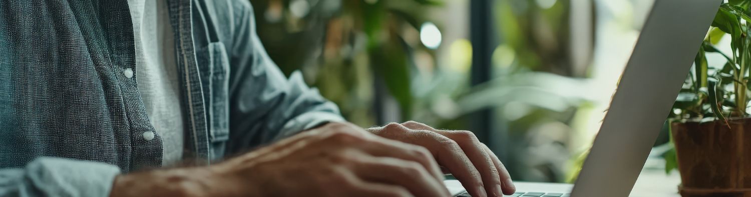 Close-up of hands typing on a laptop with lush green plants in the background, symbolizing creative blogging in a relaxed, natural setting.