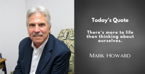 A portrait of Mark Howard sitting in a chair with a patterned cushion, wearing a navy blue blazer and white shirt, smiling. To the right, a quote in white text on a dark background reads: "There's more to life than thinking about ourselves." Below the quote, his name is displayed in white capital letters.