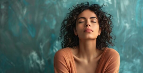 Woman with eyes closed, gently breathing in stillness against a soft teal background