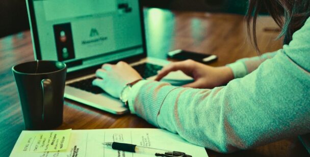 Hands typing on a laptop with handwritten notes and coffee, showing how business structure supports clarity and consistency